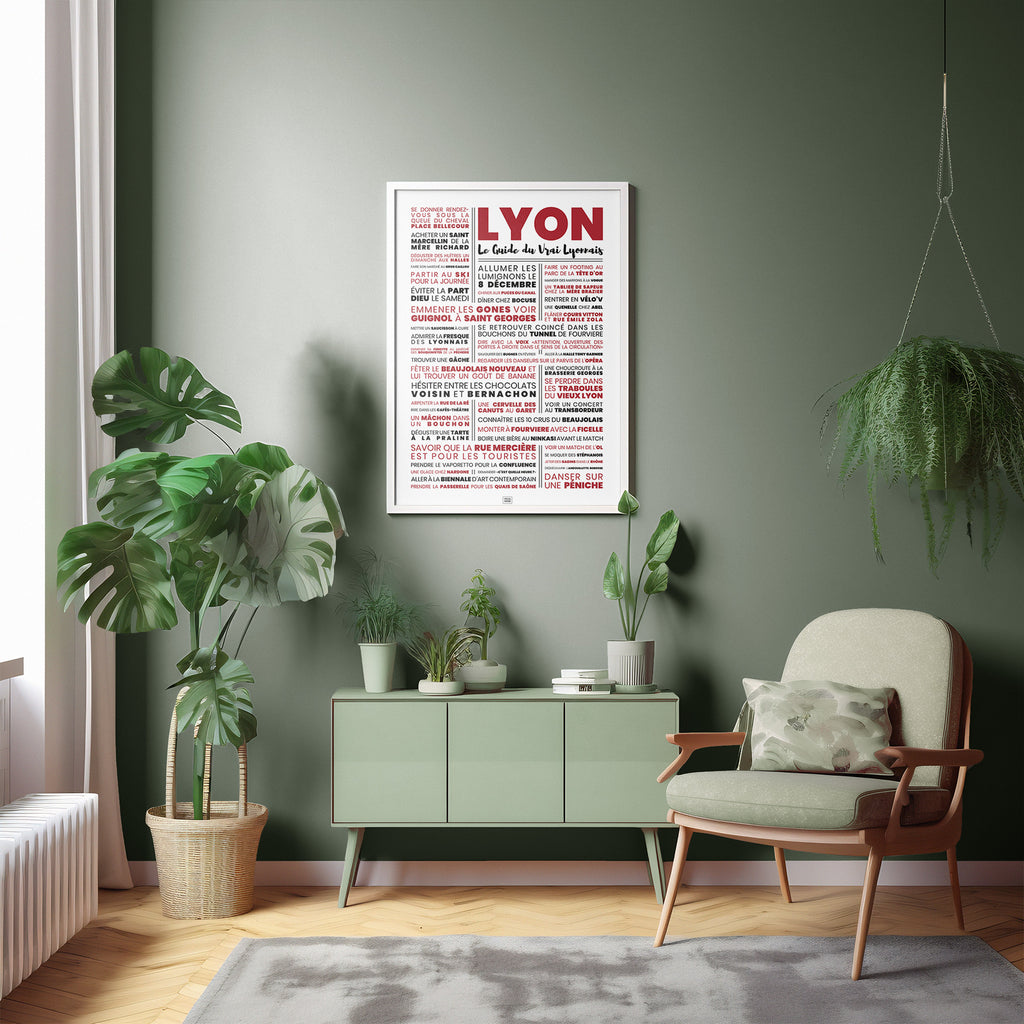 Affiche Lyon Le Guide du Vrai Lyonnais encadrée 50×70 cm accrochée dans un salon vert sauge avec fauteuil scandinave et monsteras