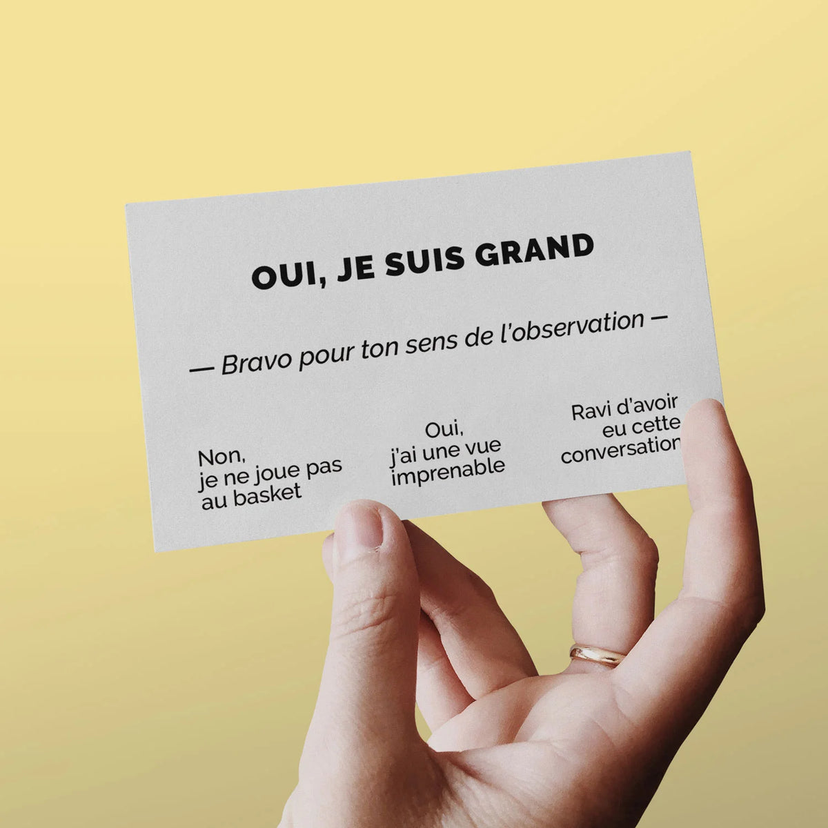 Main tenant une carte de visite « Oui, je suis grand » sur fond jaune