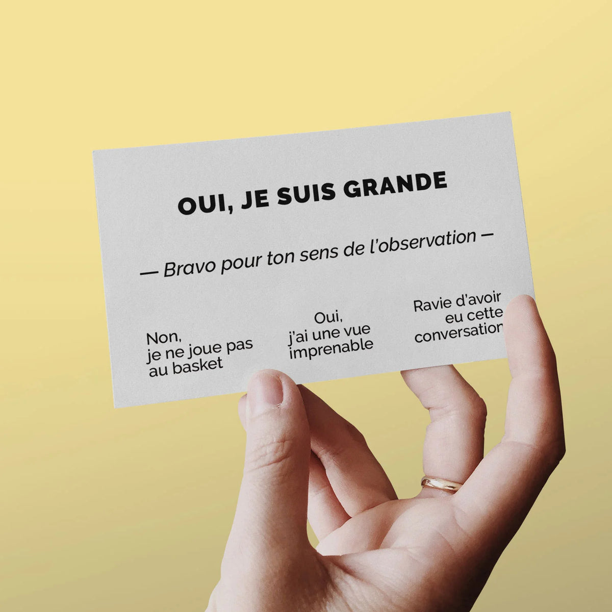 Main tenant une carte de visite « Oui, je suis grande » sur fond jaune