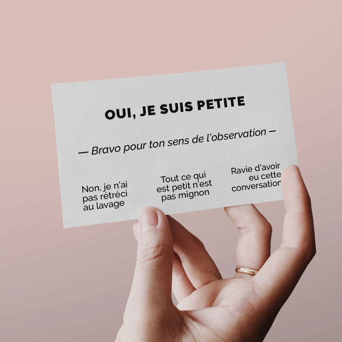 Main tenant une carte de visite « Oui, je suis petite » sur fond rose