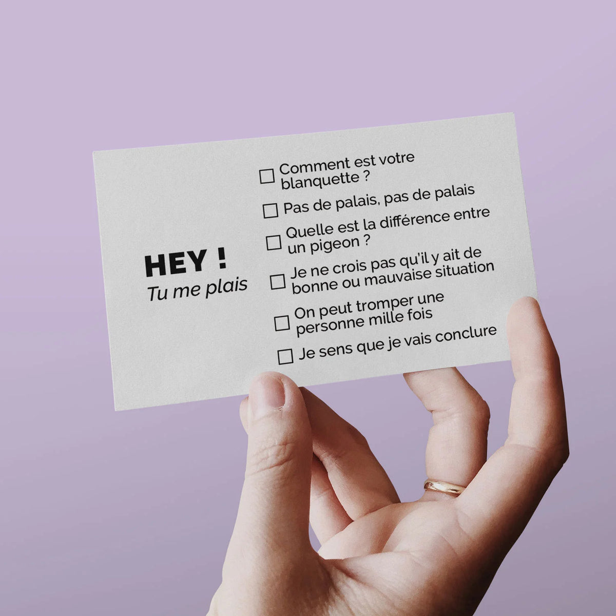 Main tenant une carte de visite séduction spécial boomer « Hey ! Tu me plais » sur fond lilas