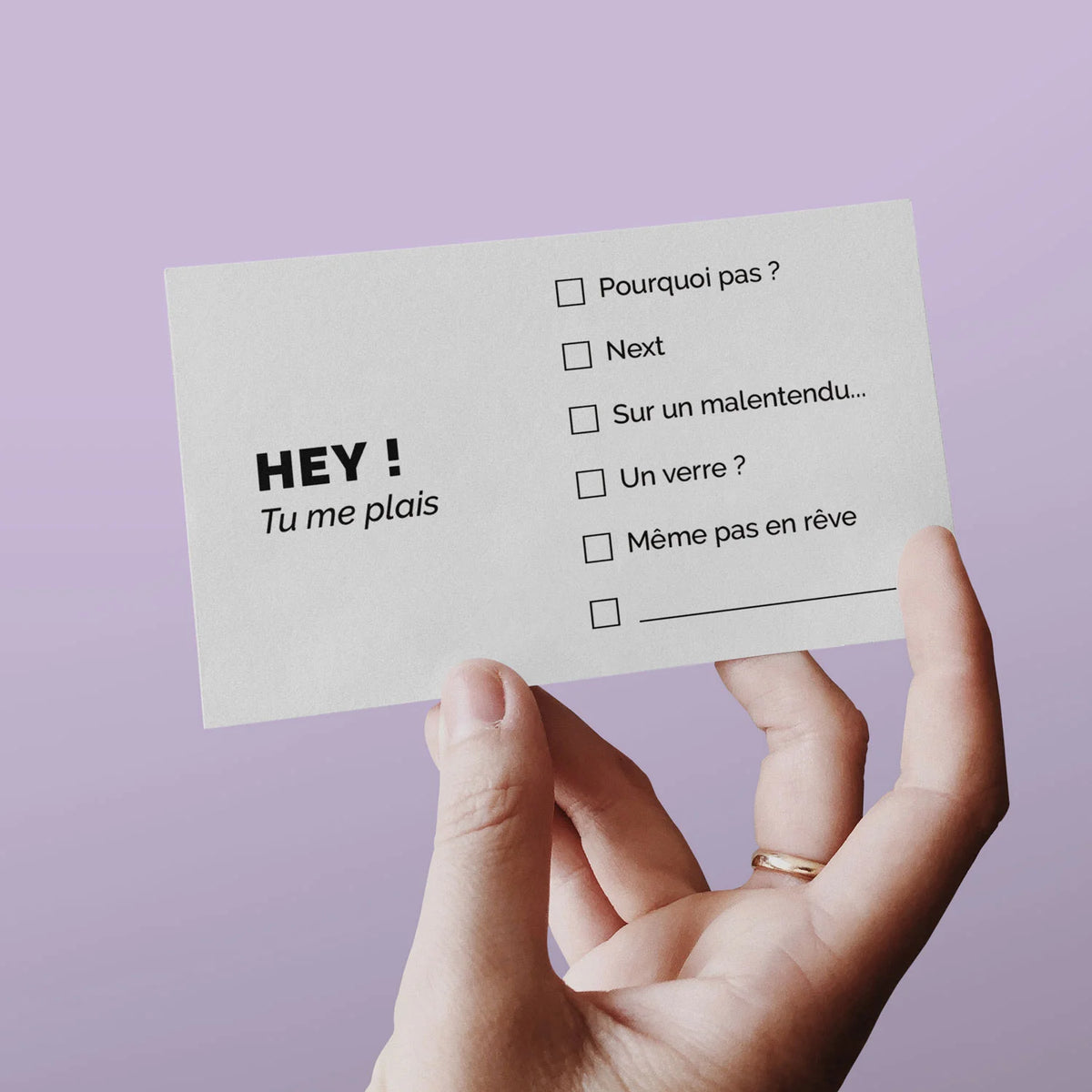 Main tenant une carte de visite « Hey ! Tu me plais » sur fond lilas
