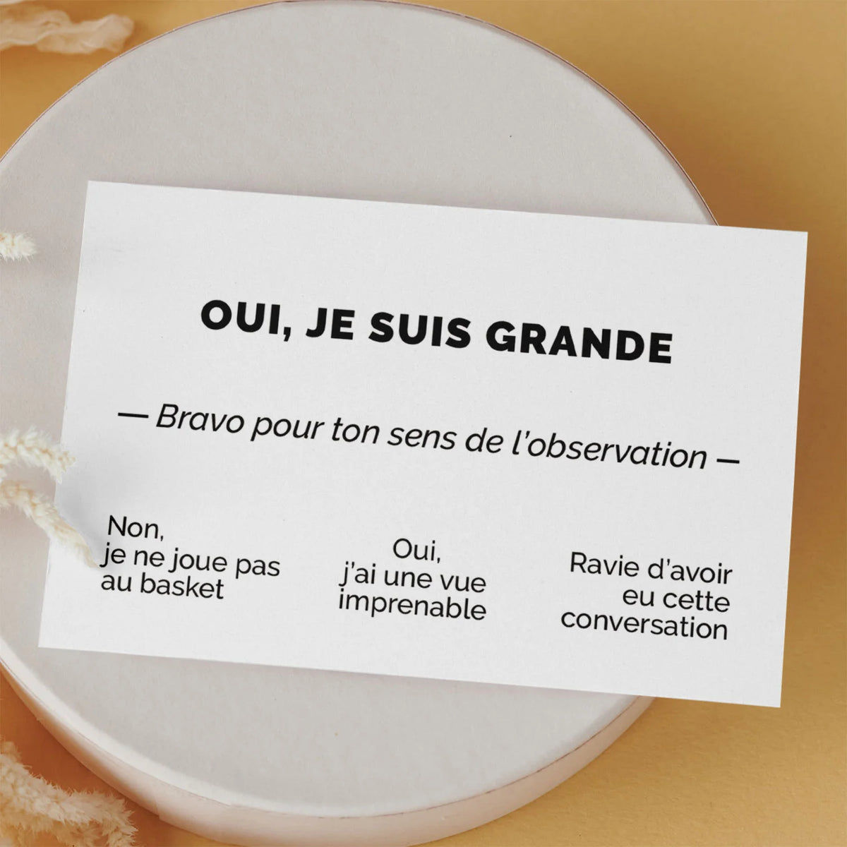 Carte de visite drôle « Oui, je suis grande » posée sur une boîte ronde, fond orange